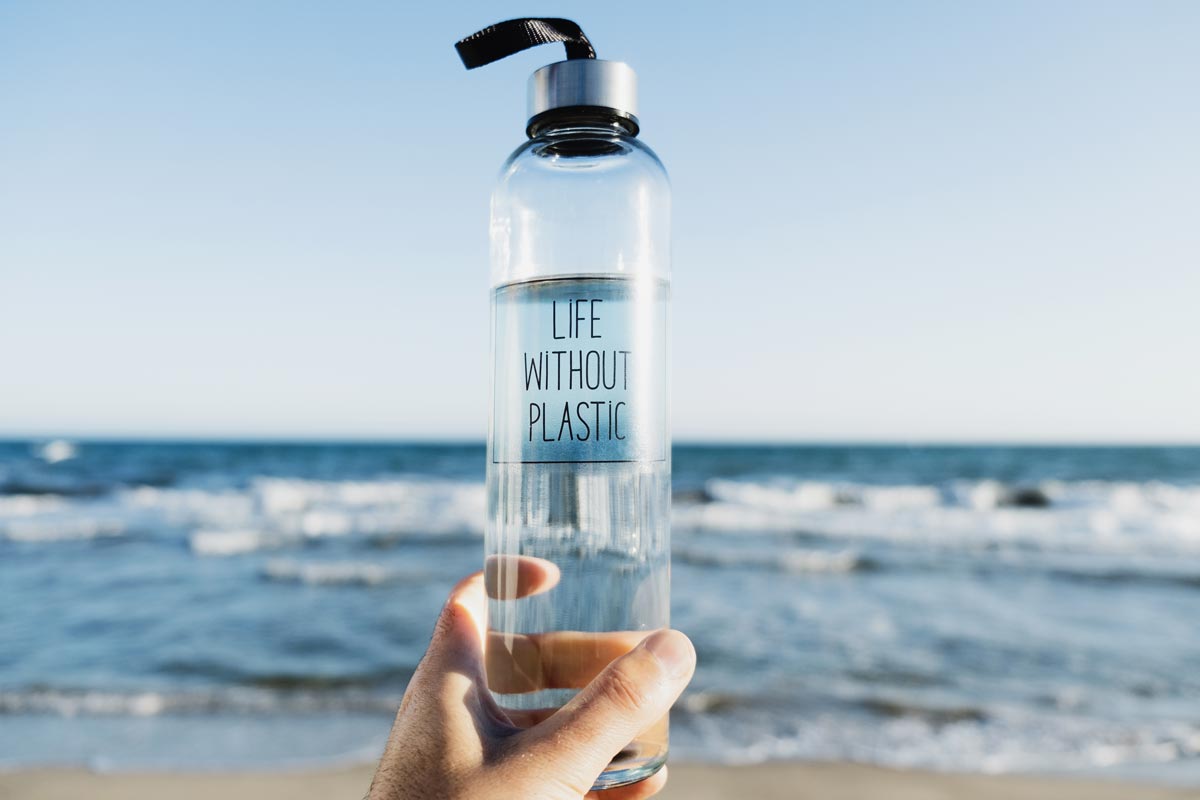 Trinkflasche ohne Plastik wird am Strand in der Hand gehalten